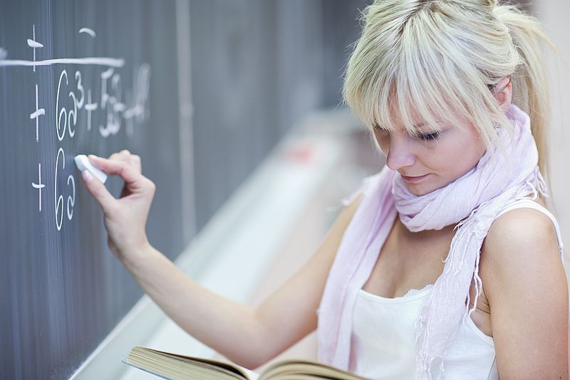 Eine junge Frau löst mathematische Gleichungen an einer Tafel 